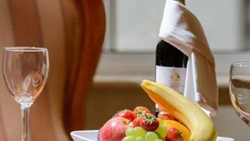 A dining table with a bowl of fruit, a bottle of wine, and a glass of wine.
