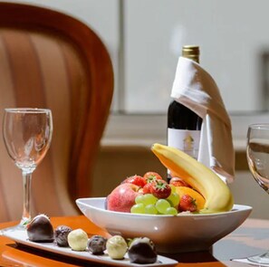 A dining table with a bowl of fruit, a bottle of wine, and a glass of wine.