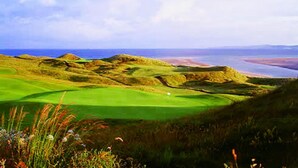 Campo de golf con un green, un cuerpo de agua y colinas al fondo.