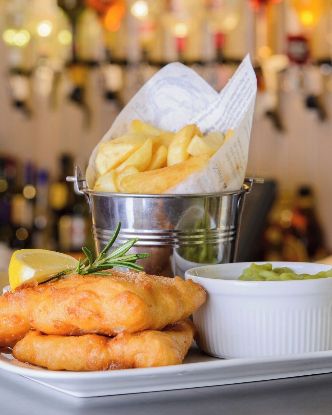 A plate with fish and chips, a small bowl of tartar sauce, and a container of fries.