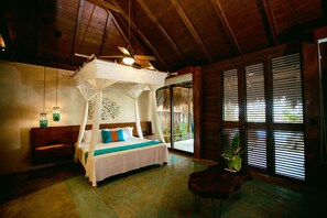 A four-poster bed with a canopy, a bench, a chair, and a large window with blinds.
