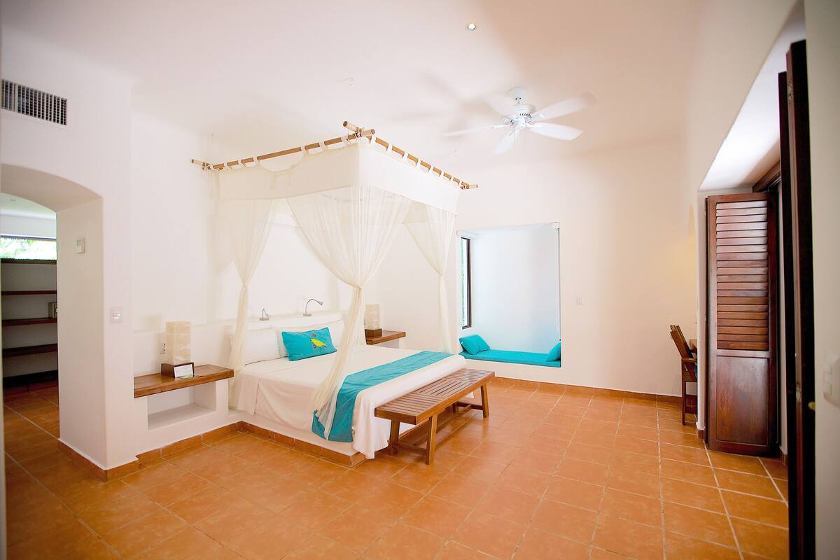 A bedroom with a four-poster bed, a ceiling fan, and a view of the outside.