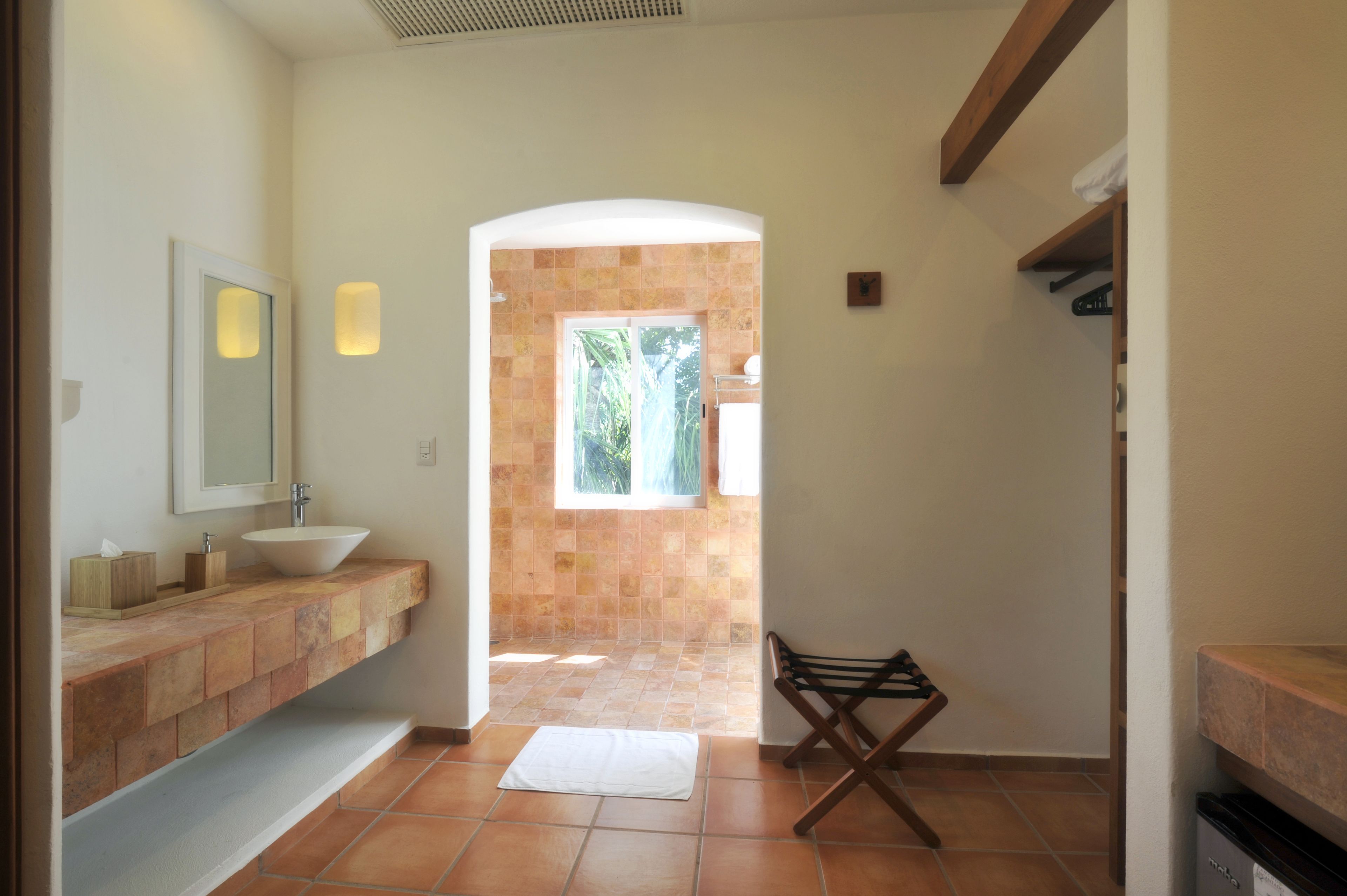 A bathroom with a white sink, a mirror, and a tiled floor. There is a window with a view of greenery outside.