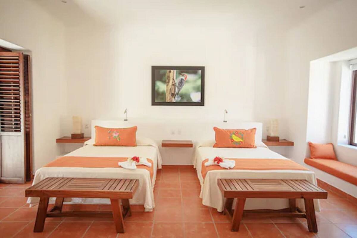A hotel room with two beds, a wooden bench, a framed picture on the wall, and a window with a view.
