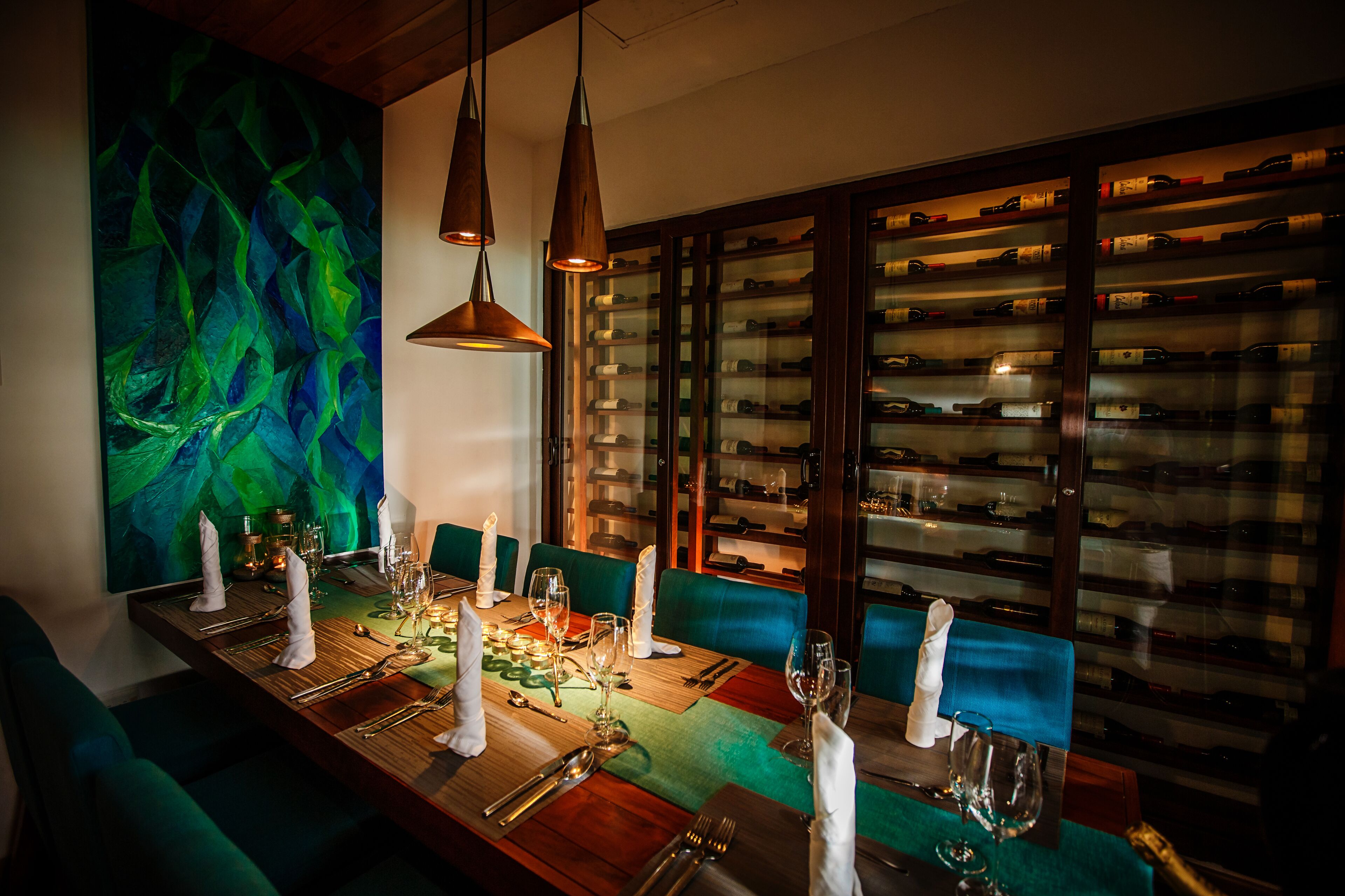 A dining area with a long table set for a meal, a wine rack in the background, and a vibrant abstract painting on the wall.