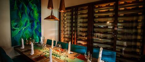 A dining area with a long table set for a meal, a wine rack in the background, and a vibrant abstract painting on the wall.
