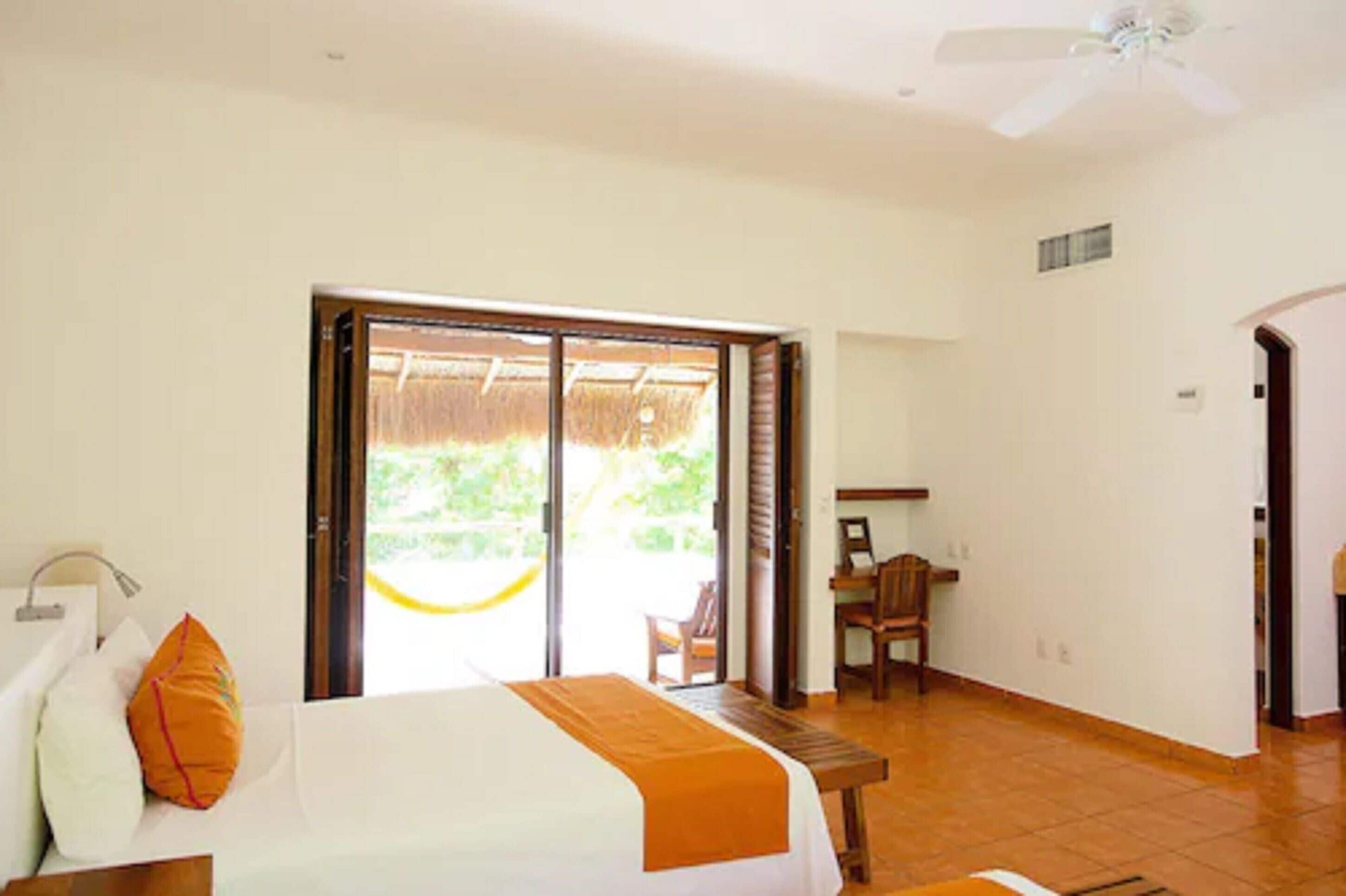 A hotel room with a bed, a desk, a chair, and a large sliding glass door leading to an outdoor area.
