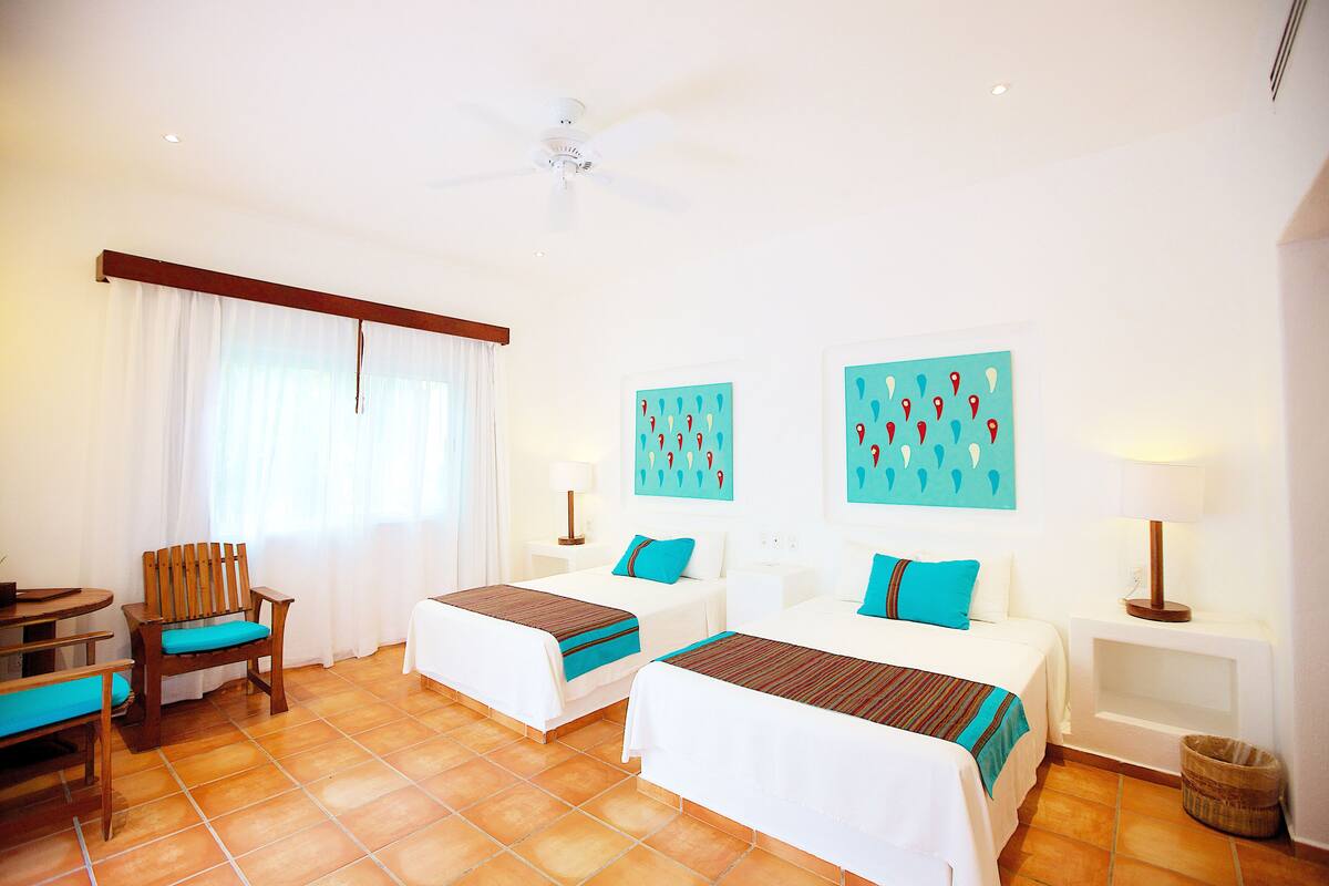 A hotel room with two beds, a desk, a chair, and a ceiling fan.