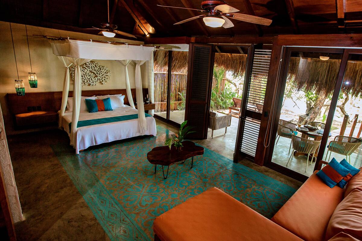 A room with a four-poster bed, a sofa, a coffee table, and a balcony with chairs.
