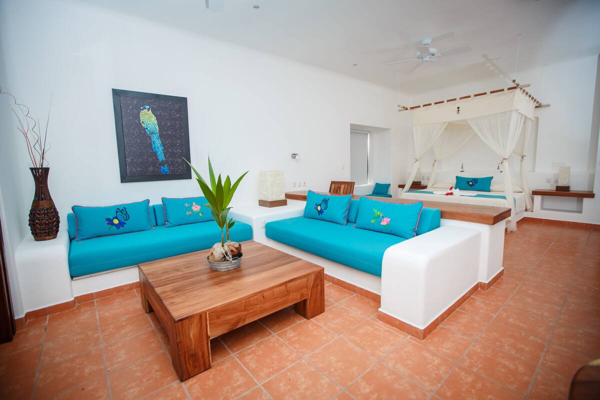 A modern living room with a wooden coffee table, blue sofas, and a white canopy bed.