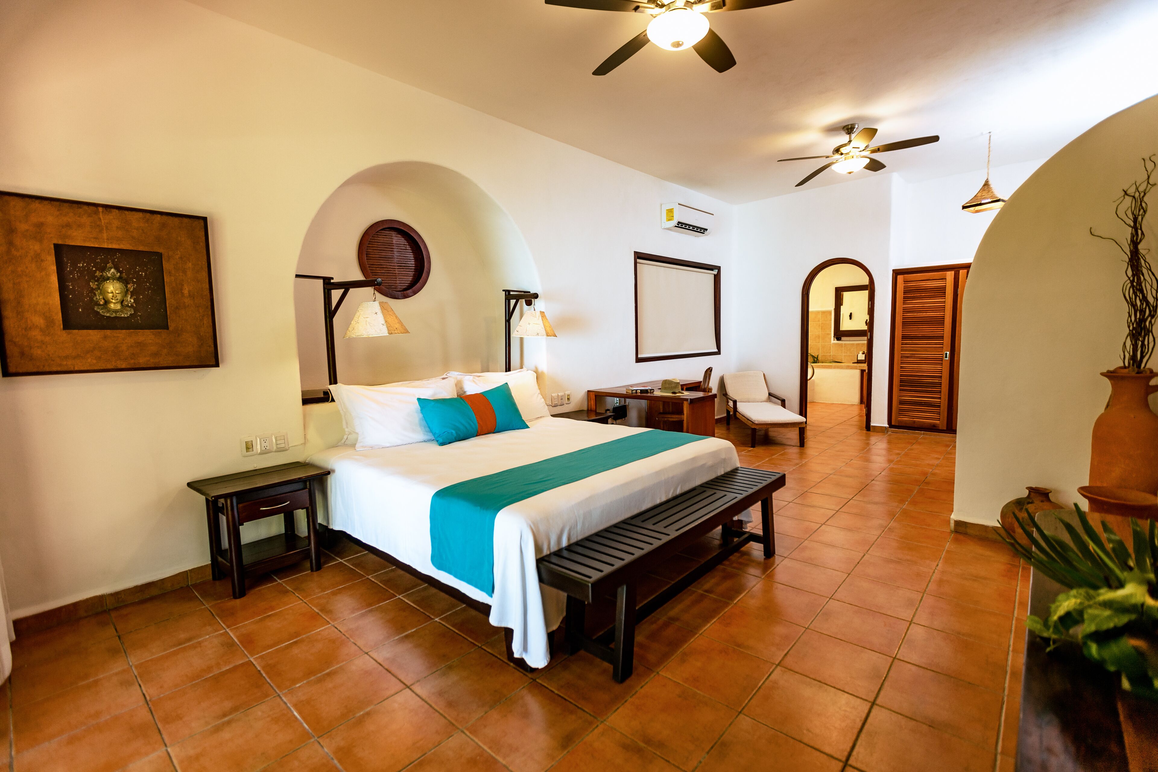 Ein Hotelzimmer mit Bett, Bank, Schreibtisch, Stuhl und Deckenventilator.