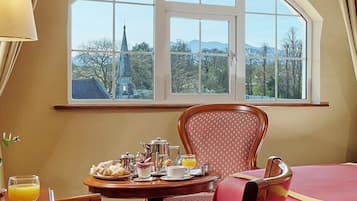 Habitación de hotel con un ventanal arqueado grande, una mesa de comedor con desayuno y una cama con colcha roja.