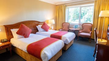A hotel room with two beds, a desk, a chair, and a window with curtains.