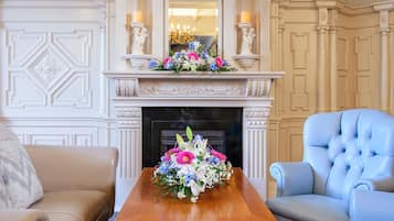 A room with a fireplace, a floral arrangement on a table, a blue armchair, and a beige sofa.