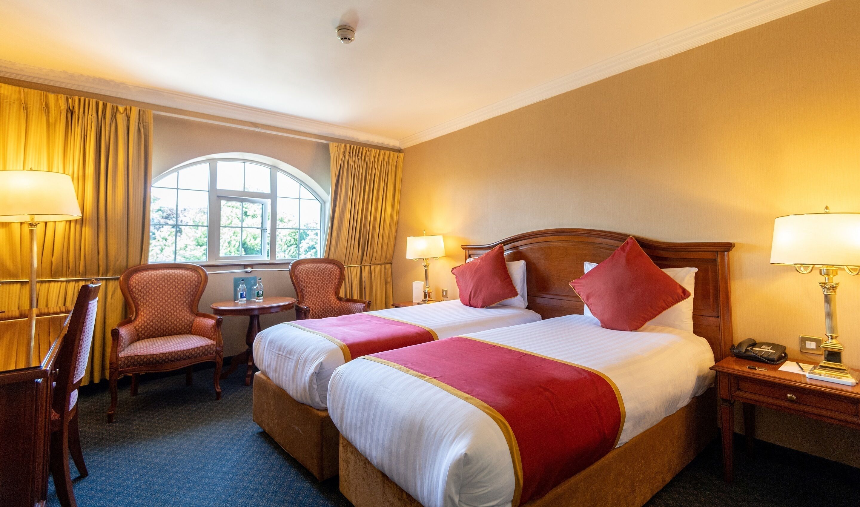 A hotel room with two beds, a desk, a chair, and a window with curtains.