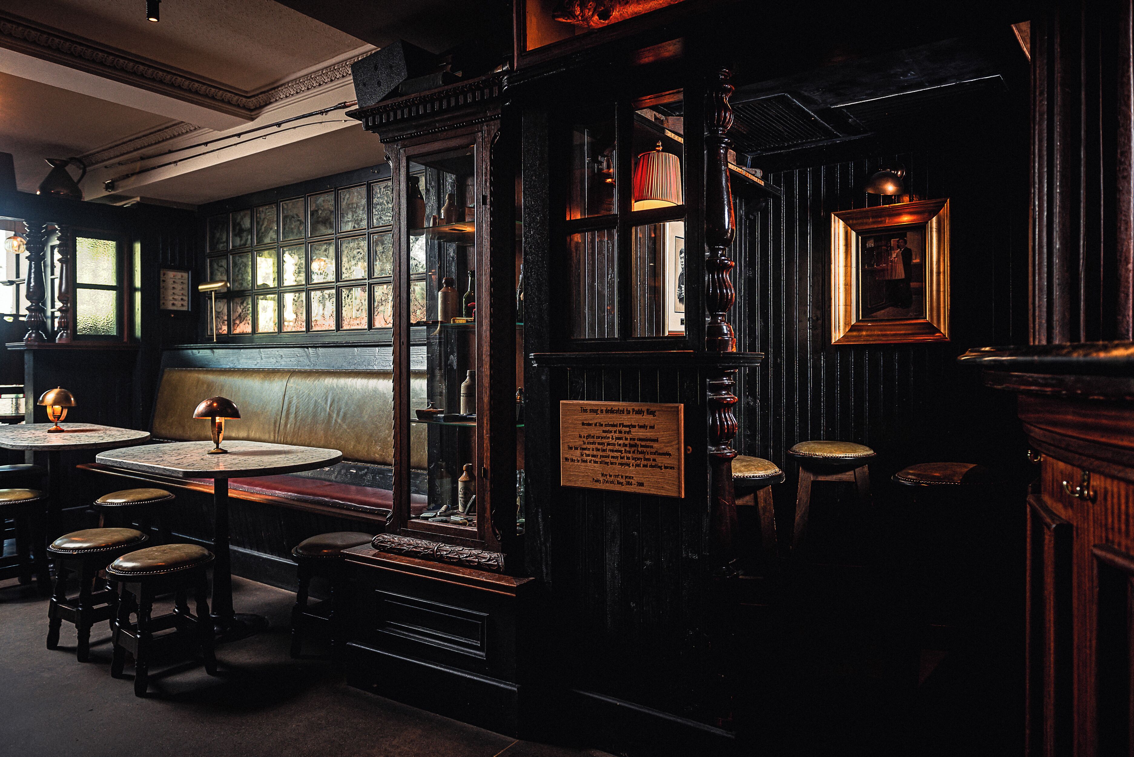 A dimly lit room with wooden walls, a bench, and a table with a lamp.
