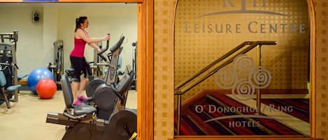 A gym area with exercise equipment and a person using a treadmill. There is a sign for the gymnasium and a window with the text "KTH Leisure Centre O'Donoghue Hotels".