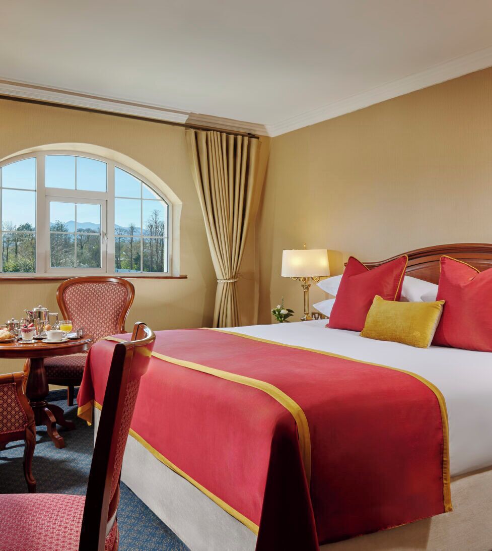 Habitación de hotel con una cama grande, una mesa de comedor, una silla y un ventanal con cortinas.