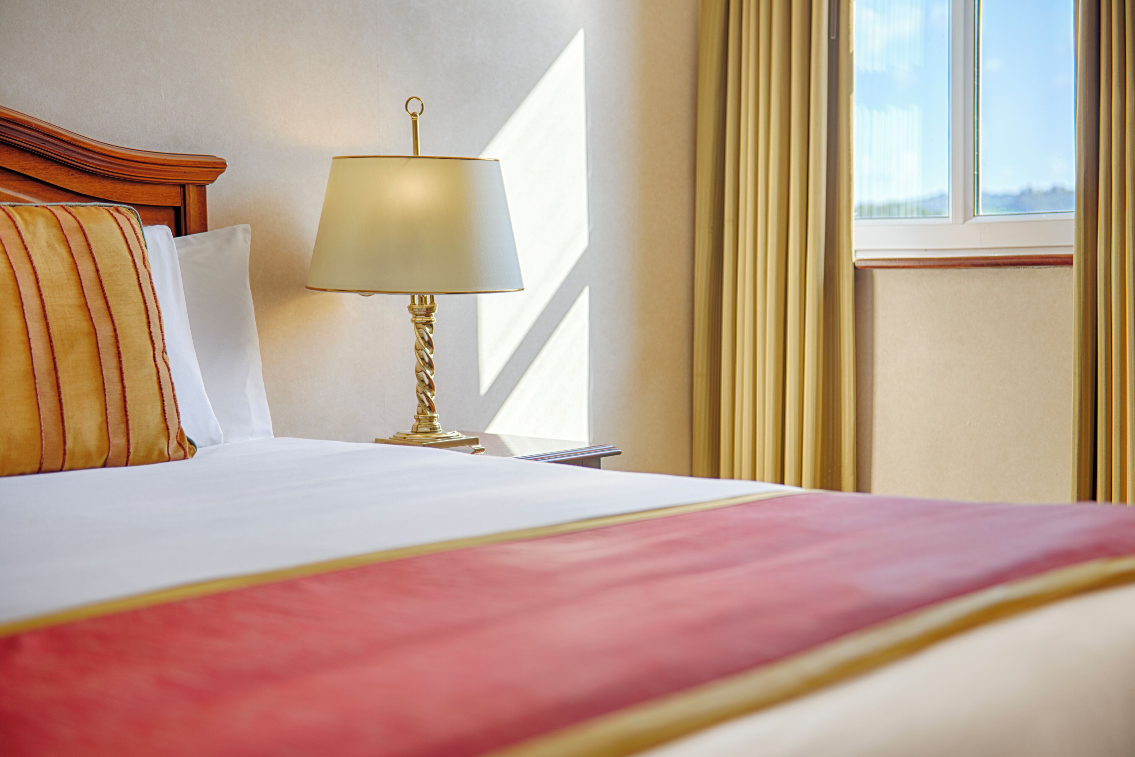 Una habitación de hotel con una cama, una lámpara de noche y una ventana con cortinas.