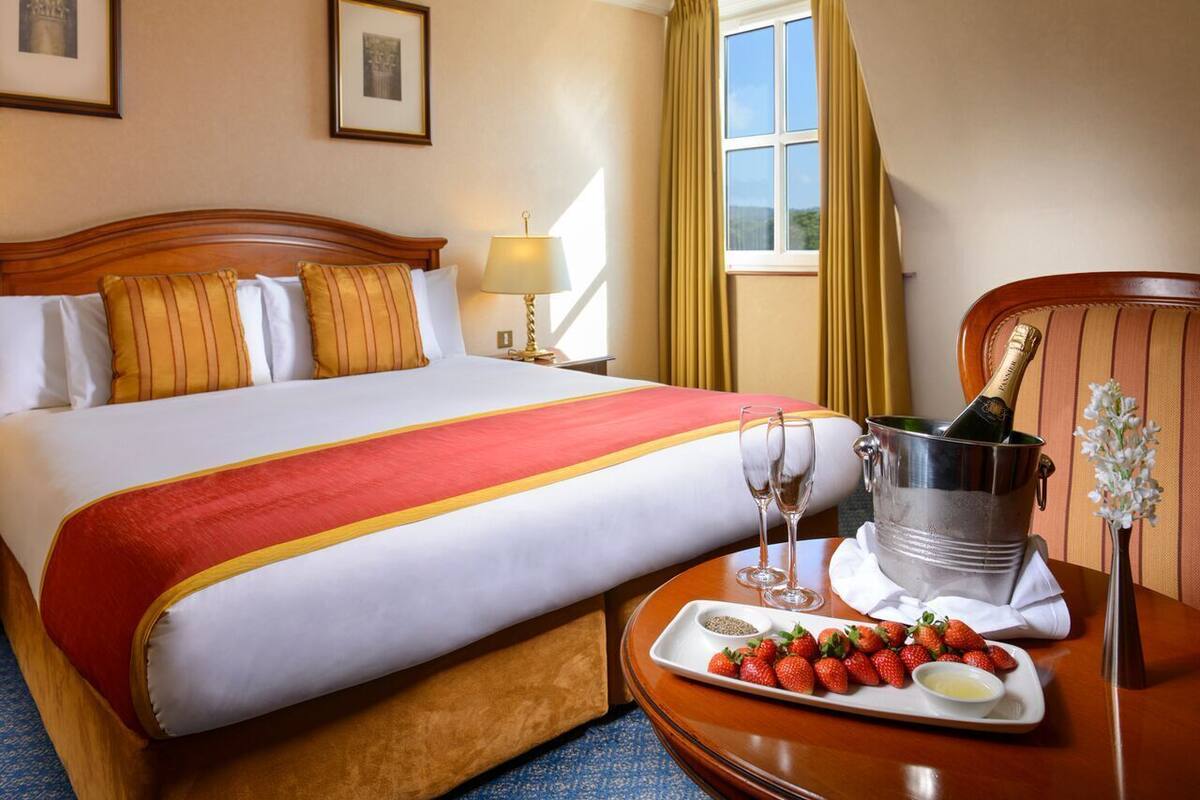Ein Hotelzimmer mit einem Bett, einer Ablage mit Erdbeeren und Champagner sowie einem Nachttisch mit einer Lampe.