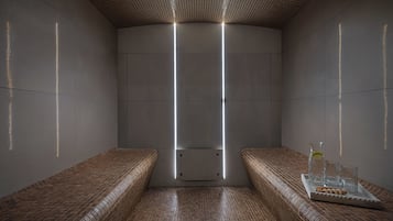 Un cuarto de spa con suelo de baldosas, bancos, una bandeja con vasos y una botella, y un techo con diseño de cuadrícula.