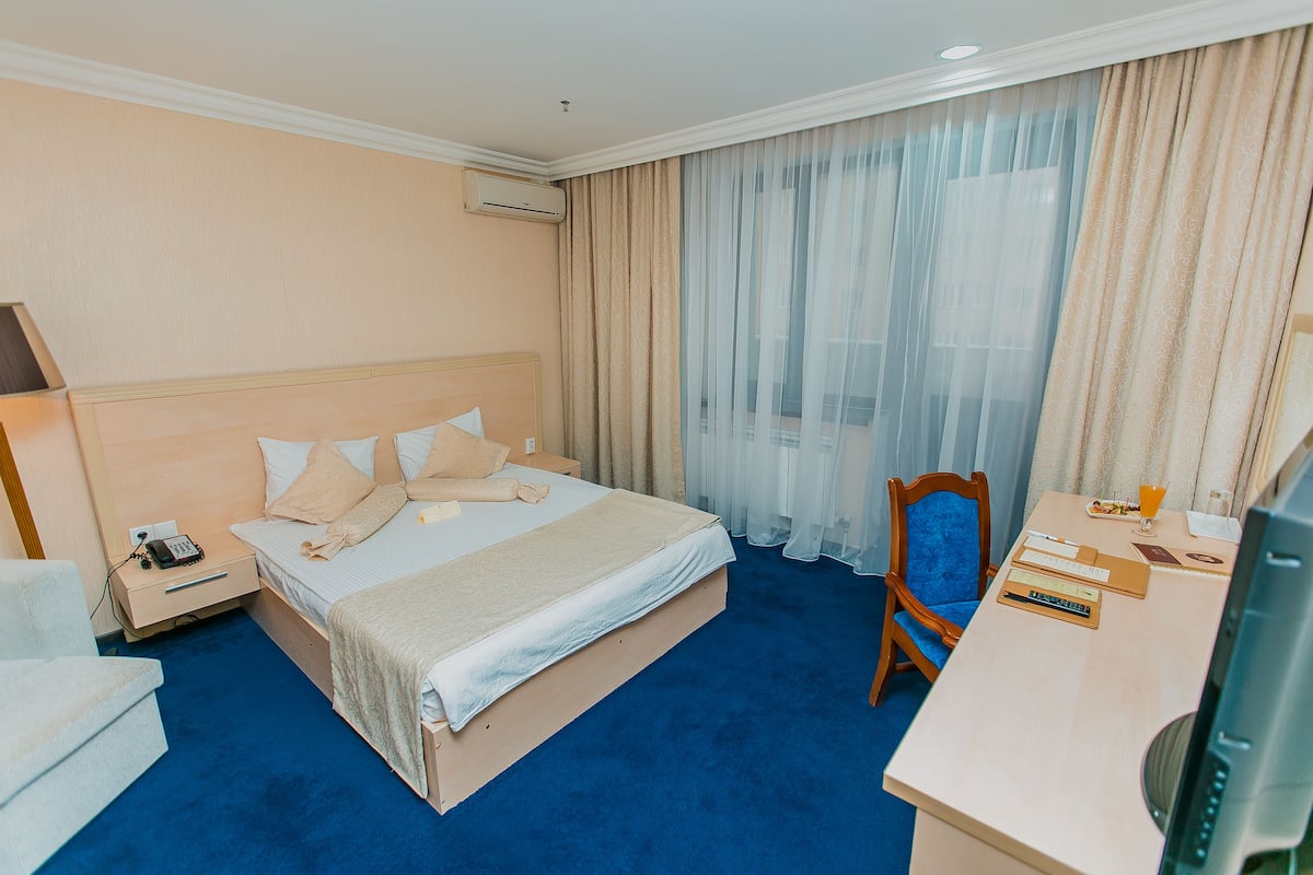 Habitación de hotel con cama, escritorio con computadora, silla y ventana con cortinas.