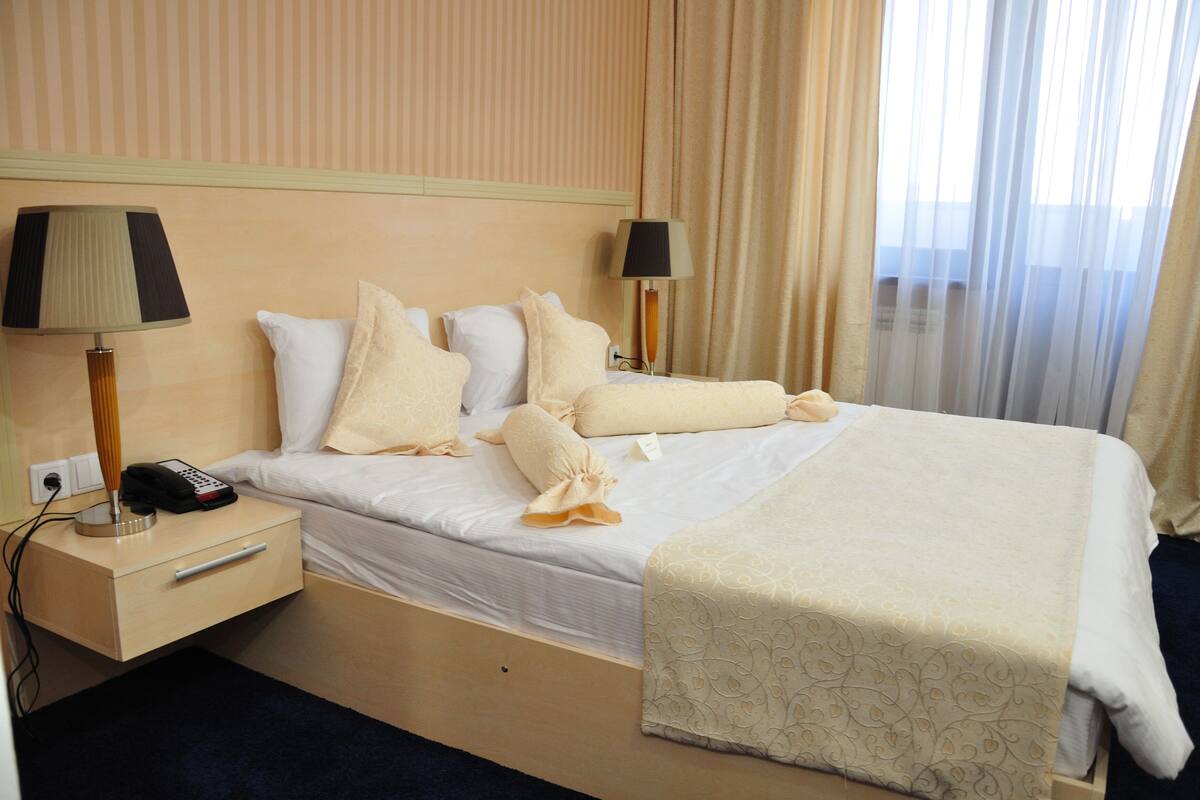 Una habitación de hotel con una cama bien hecha, dos lámparas de noche, un teléfono junto a la cama y un cajón pequeño.