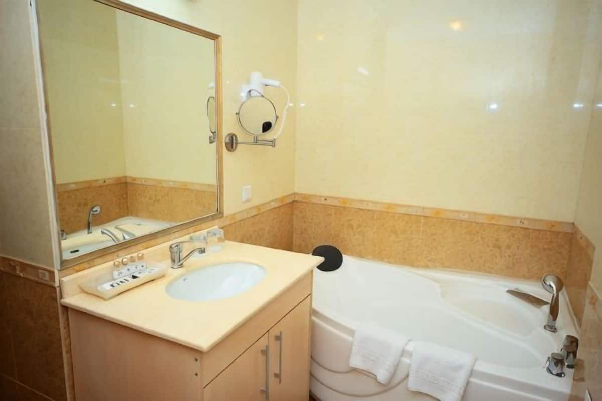 Un baño con lavamanos, espejo, toallero y bañera.