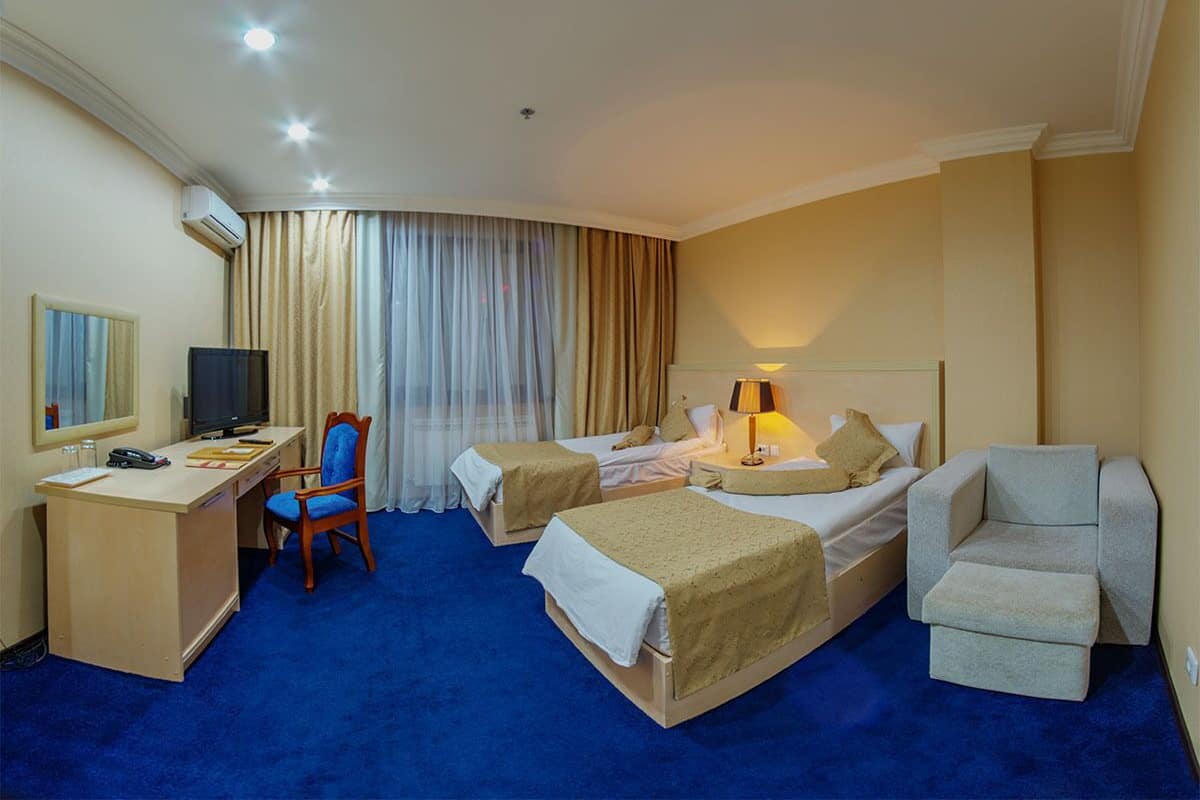 Habitación de hotel con dos camas, un escritorio con computadora, una silla y un sofá.