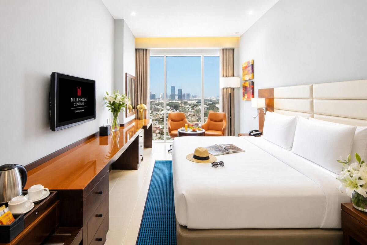 A hotel room with a bed, a desk, a TV, and a view of the city.