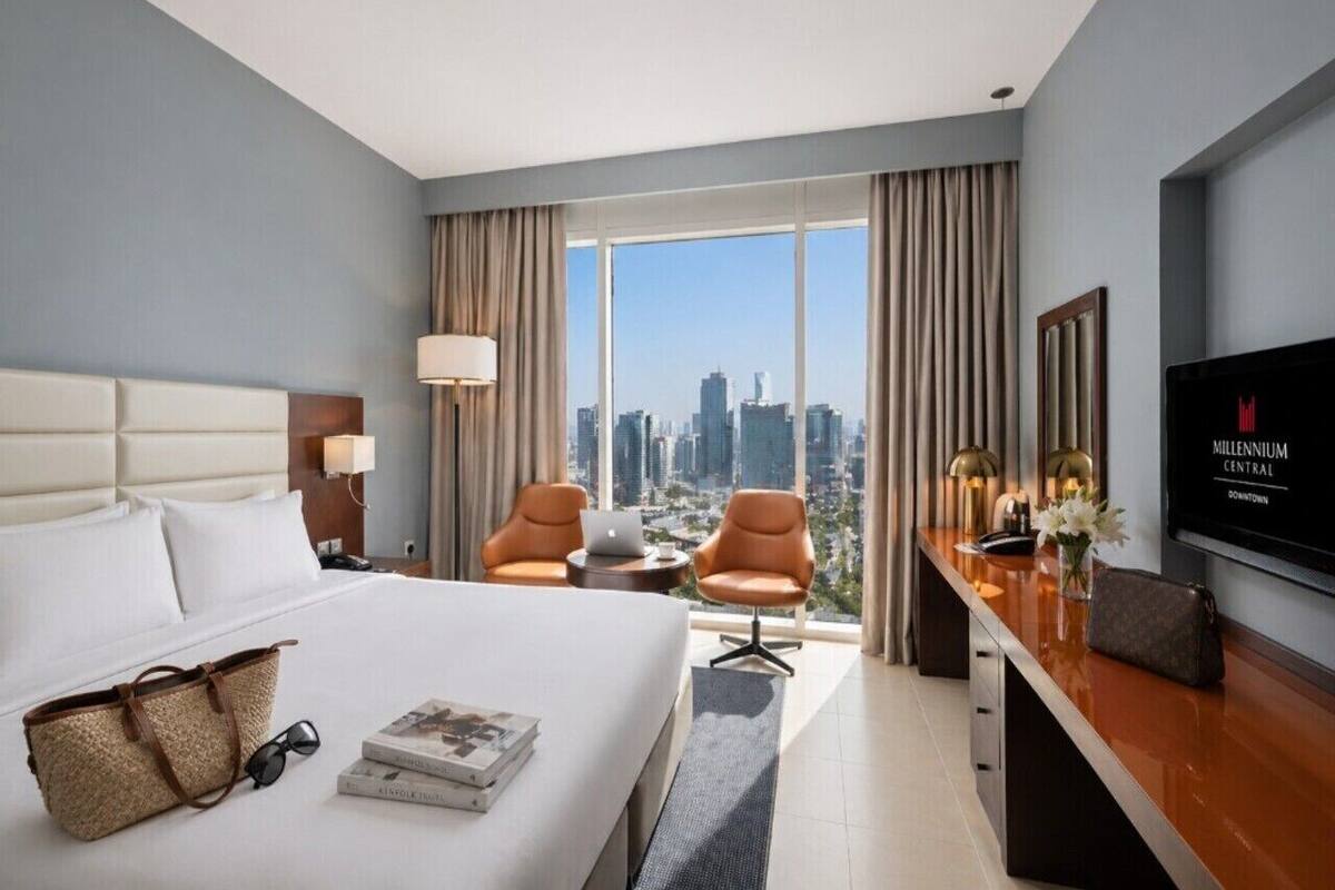 A hotel room with a bed, a desk, two chairs, a TV, and a city view.
