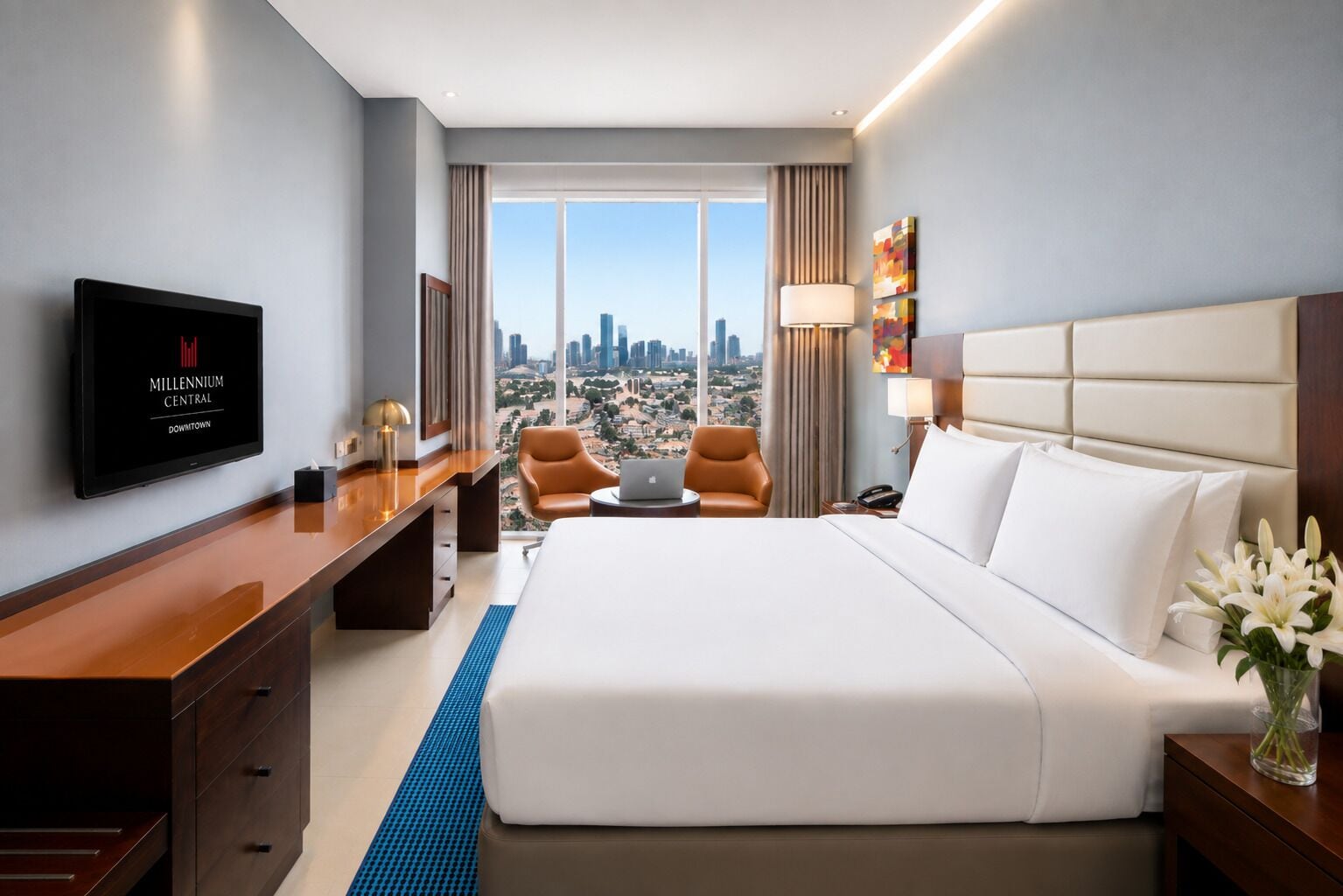 A hotel room with a large bed, a desk, a television, and a view of the cityscape.