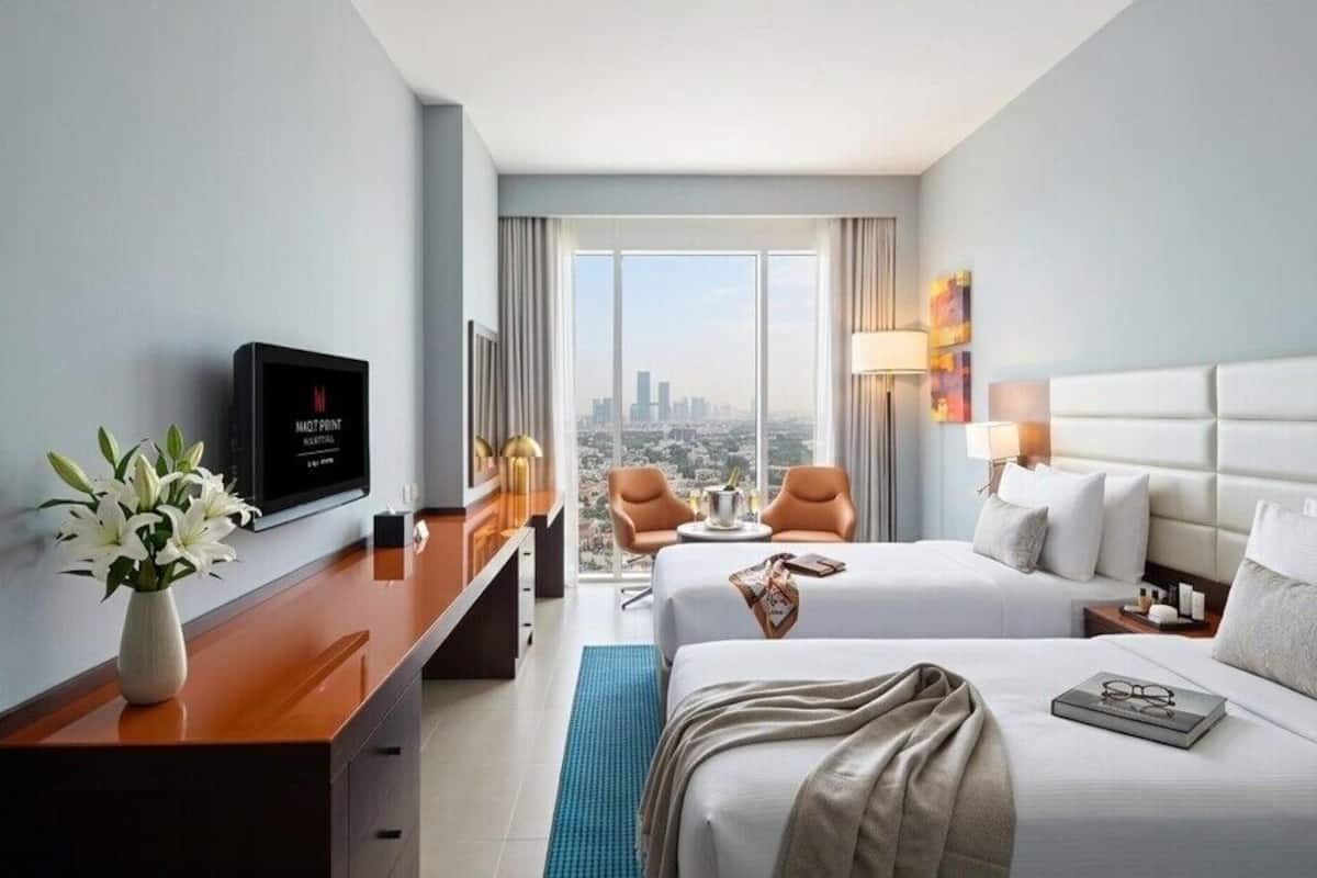 A hotel room with a bed, a desk, a TV, and a view of the city.