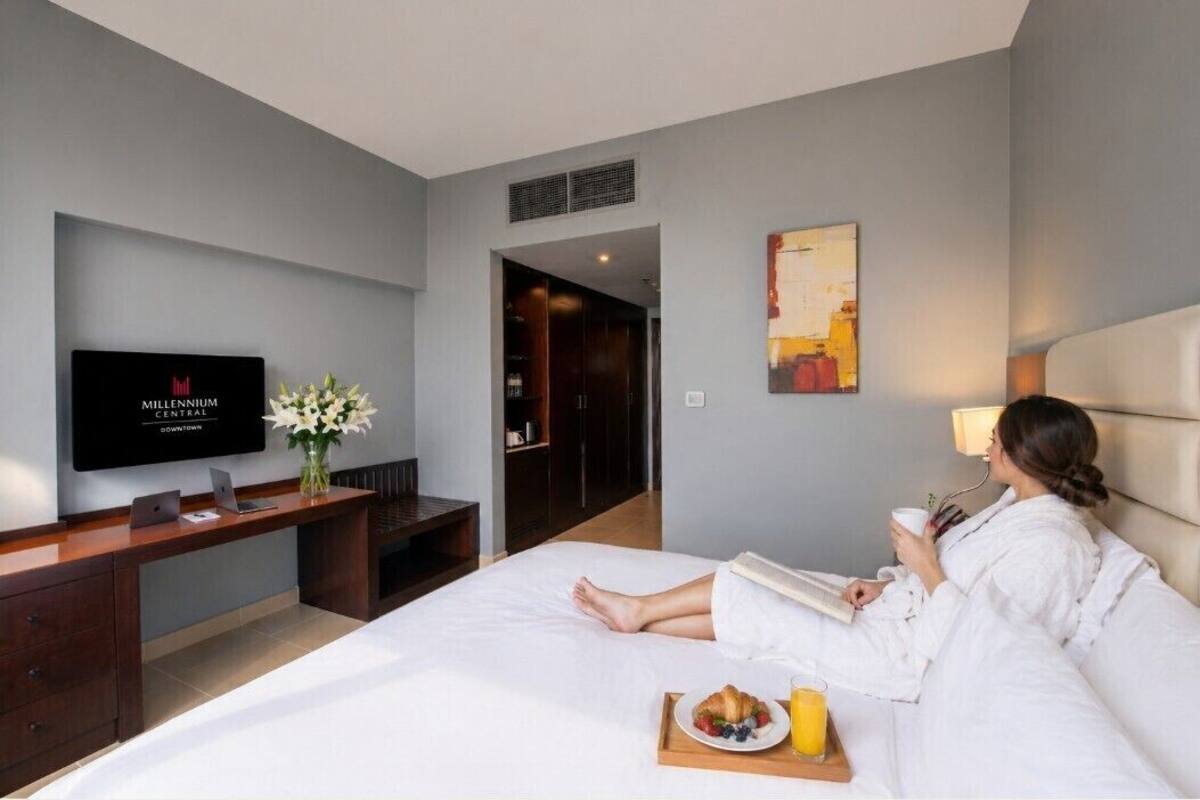 A hotel room with a bed, a desk with a laptop, a television, and a breakfast tray.