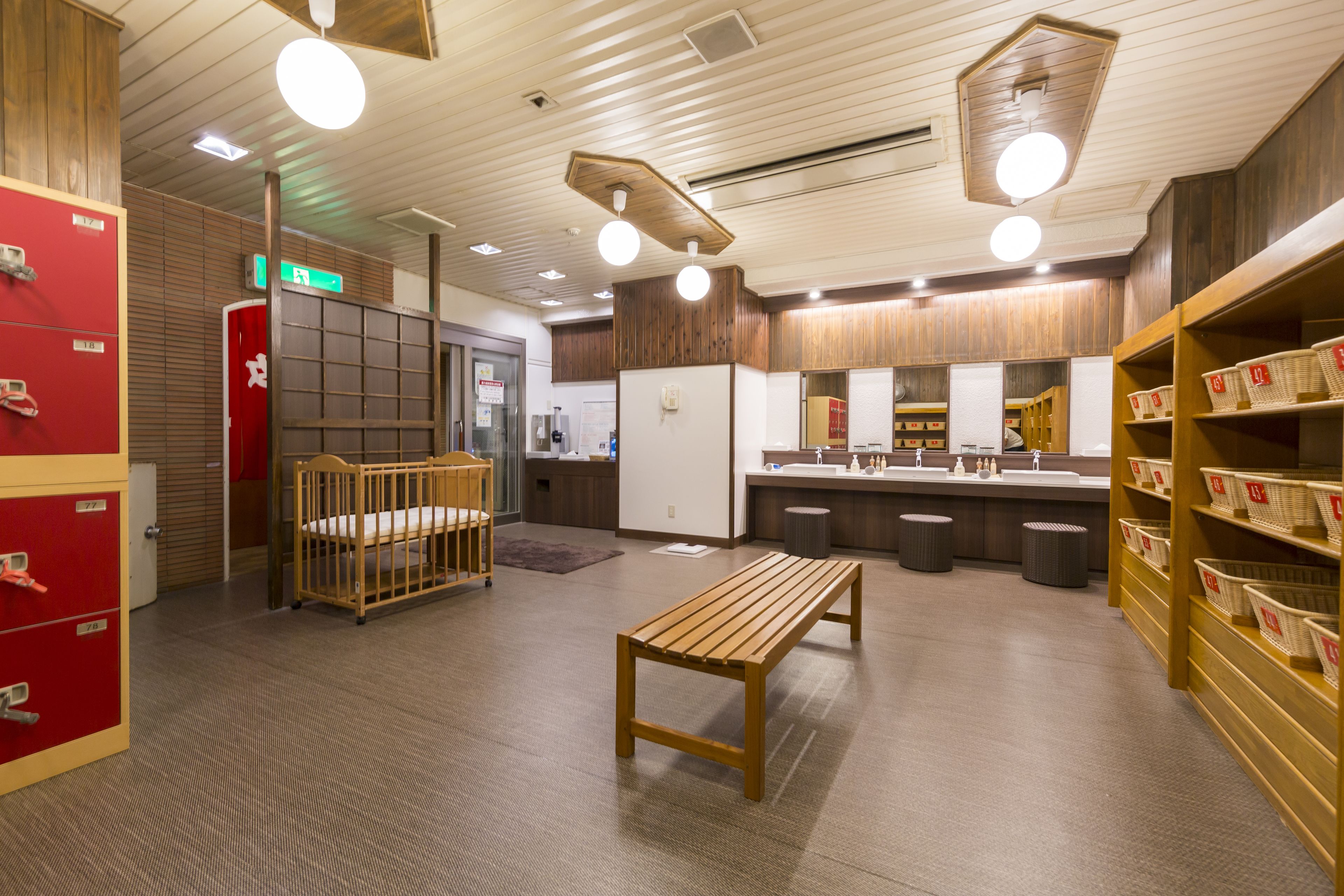 A hotel lobby with a wooden bench, a red storage unit, and a counter with baskets.