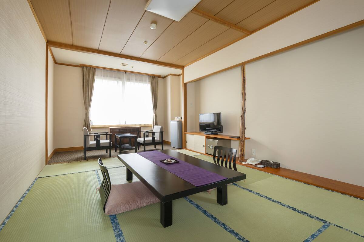 A traditional Japanese room with tatami flooring, a low table with a purple mat, a TV, and a refrigerator.