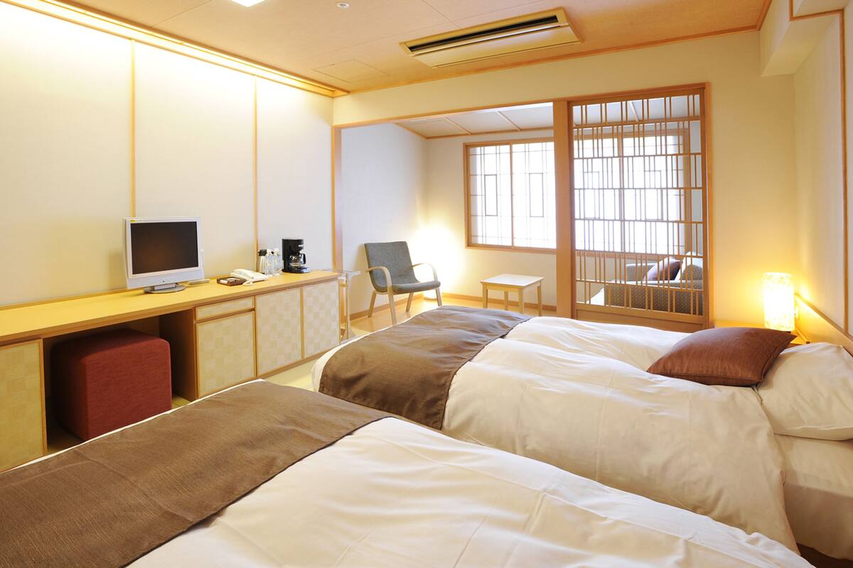 A hotel room with two beds, a desk with a computer, a chair, and a window with a view.