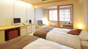 A hotel room with two beds, a desk with a computer, a chair, and a window with a view.