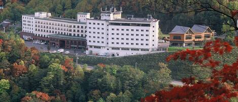 A large, multi-story building with a symmetrical facade, surrounded by dense forest.