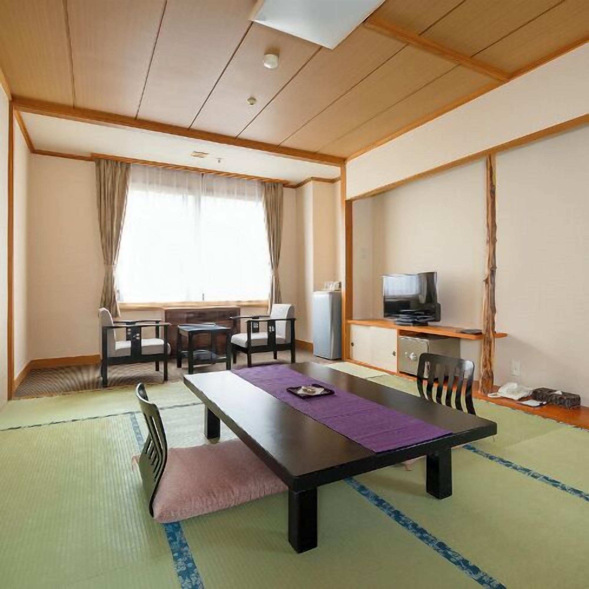 A room with a tatami mat floor, a low table with chairs, a television, and a window with curtains.