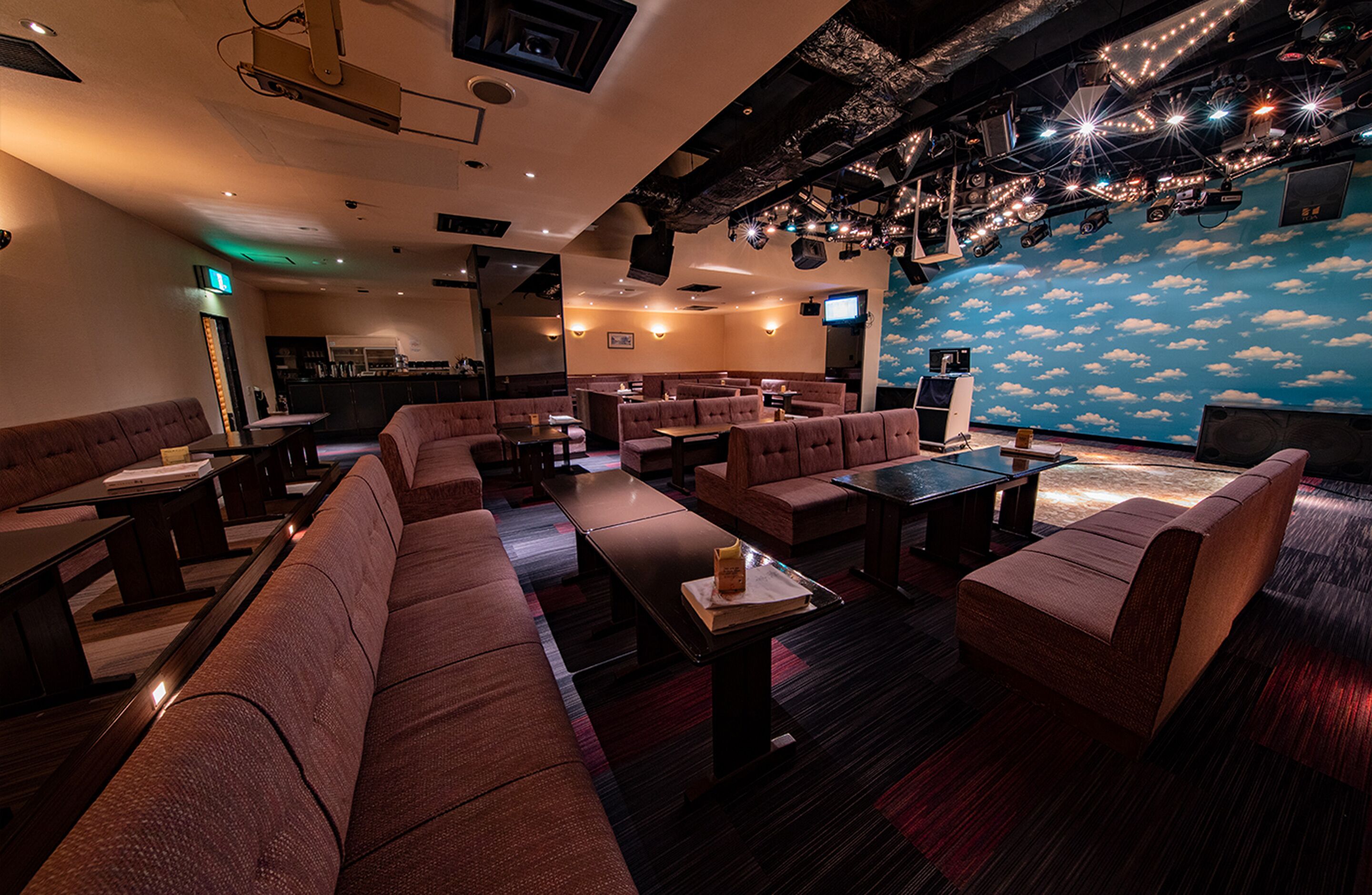 A restaurant with booths and tables, a stage with lights, and a wall with a cloud mural.