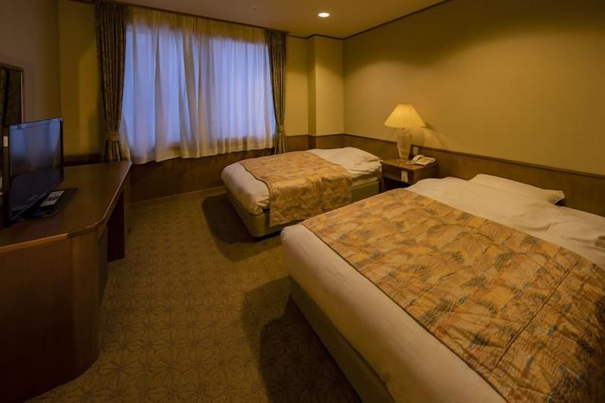 Habitación de hotel con dos camas, un escritorio, un televisor y una mesita de noche con lámpara.