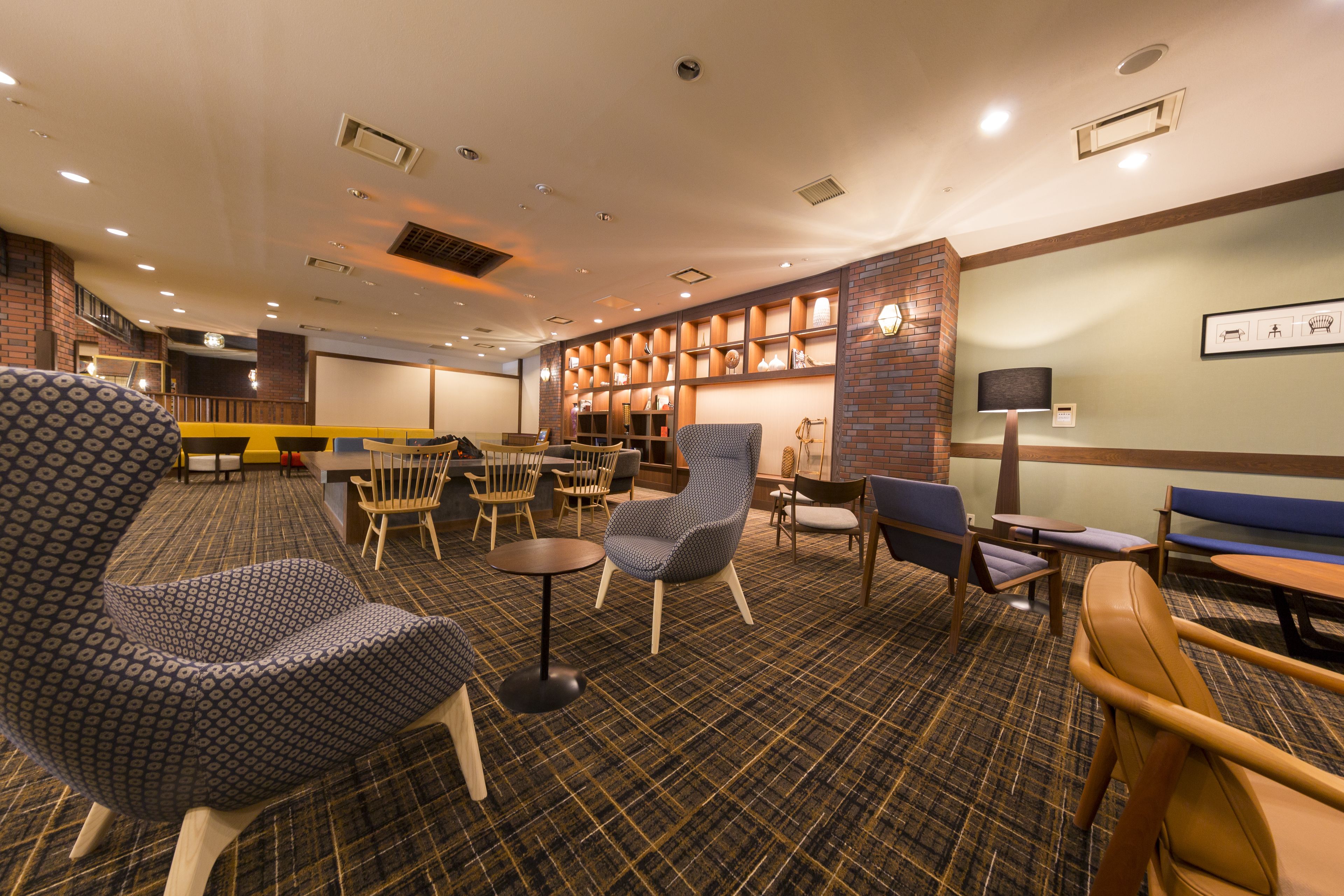 A hotel lobby with a check-in counter, seating area with chairs and tables, a fireplace, and a wall-mounted TV.