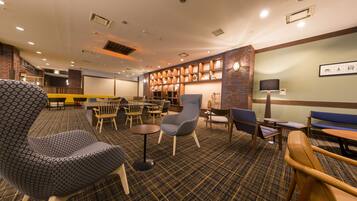 A hotel lobby with a check-in counter, seating area with chairs and tables, a fireplace, and a wall-mounted TV.