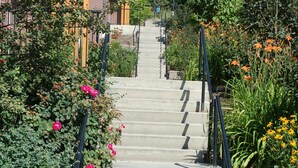 A staircase with metal railings, surrounded by greenery and flowers, leading to a building with a brick facade. - University of British Columbia - UBC Okanagan Campus (Kelowna)