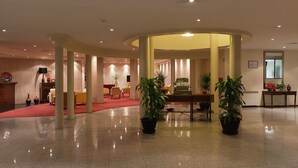 A spacious lobby with a curved ceiling, a reception desk, seating area, and potted plants. - Hotel Santa Maria (Alcobaça)