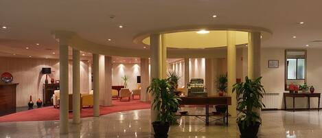 A spacious lobby with a curved ceiling, a reception desk, seating area, and potted plants.