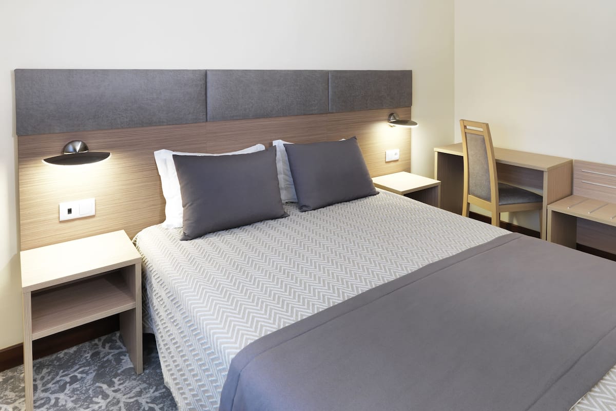 A neatly arranged hotel room with a large bed, two bedside tables, a nightstand, a chair, and a desk.