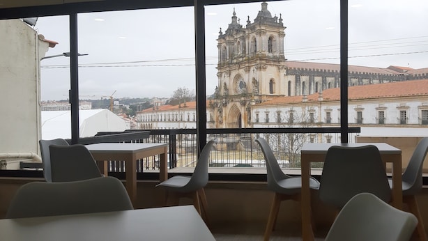 A room with a large window offering a view of a historic building with a bell tower. There are tables and chairs arranged for dining. - Hotel Santa Maria (Alcobaça)