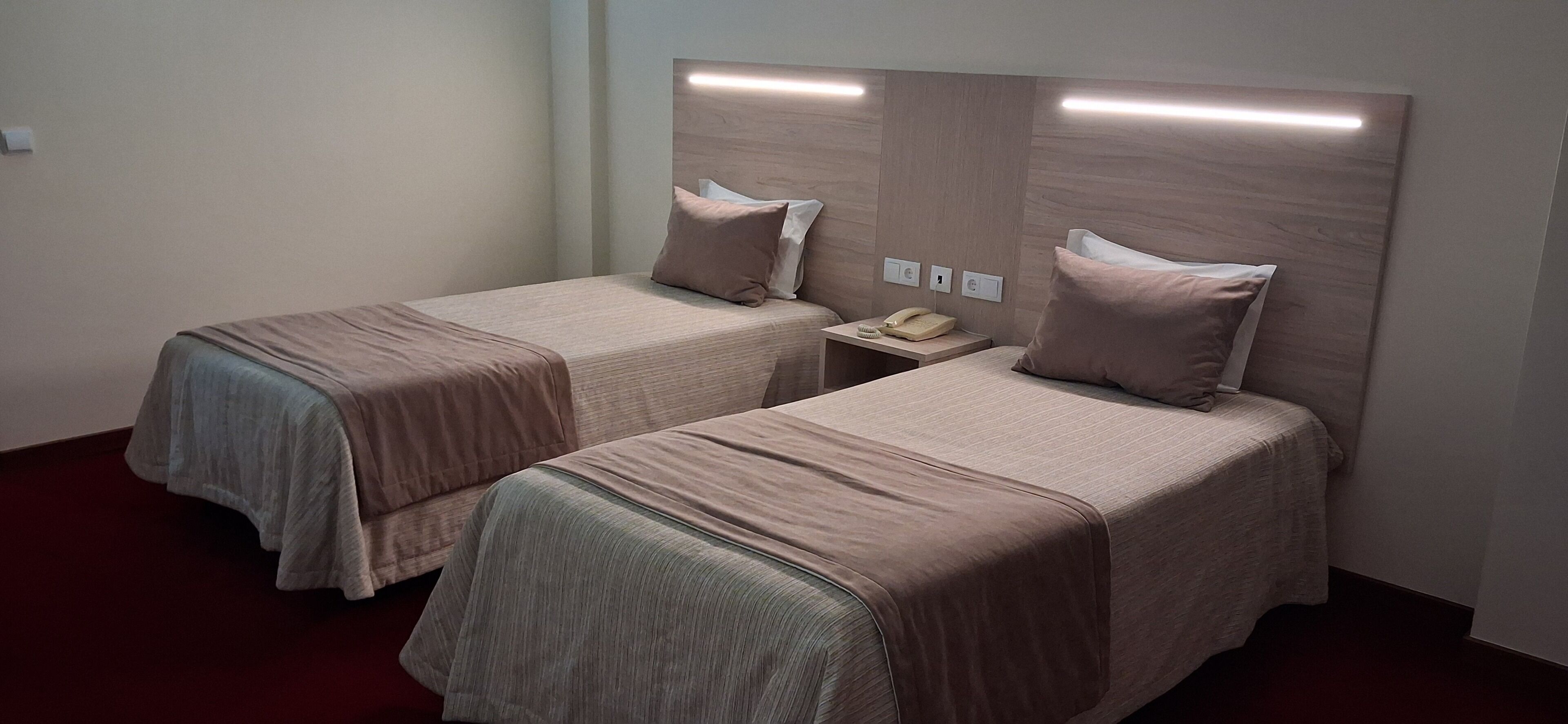 Une chambre d’hôtel avec deux lits simples, une table de chevet avec un téléphone et un luminaire fixé au mur.